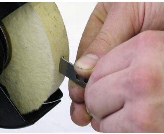 Hand holding a knife blade against a felt wheel on the knife sharpening machine